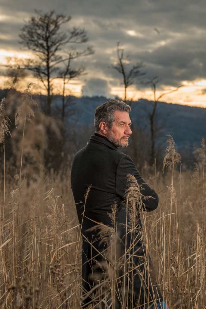 Outdoorportrait Mann im schwarzen Rollkragenpullover in bayerischer Landschaft mit dramatischem Himmel